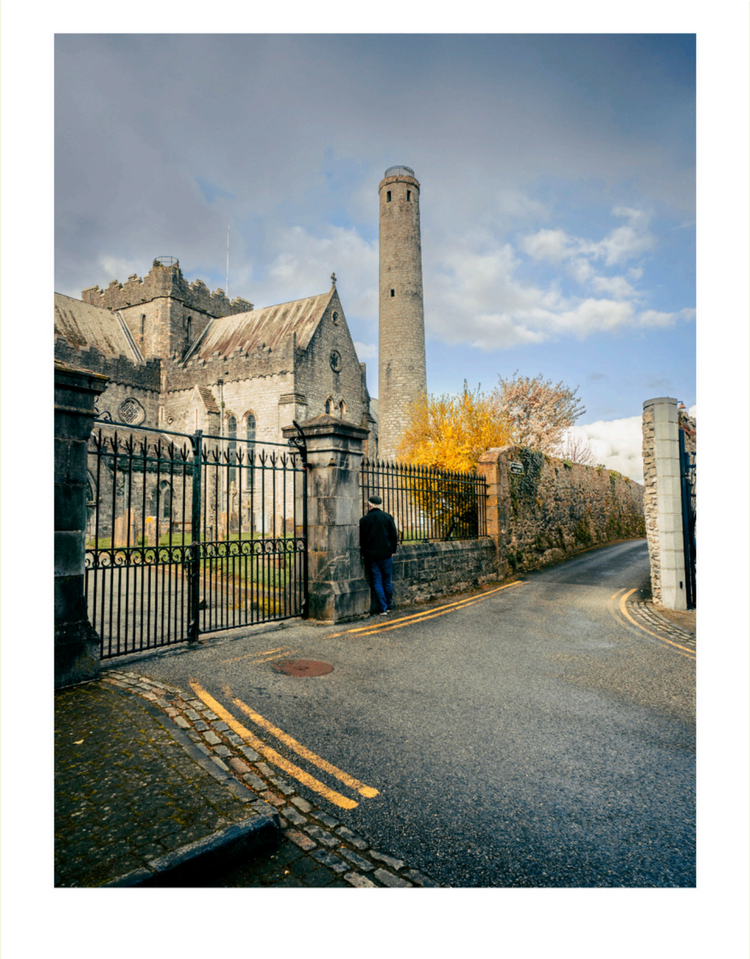 Person standing near a large stone building with a tall tower under a blue sky.