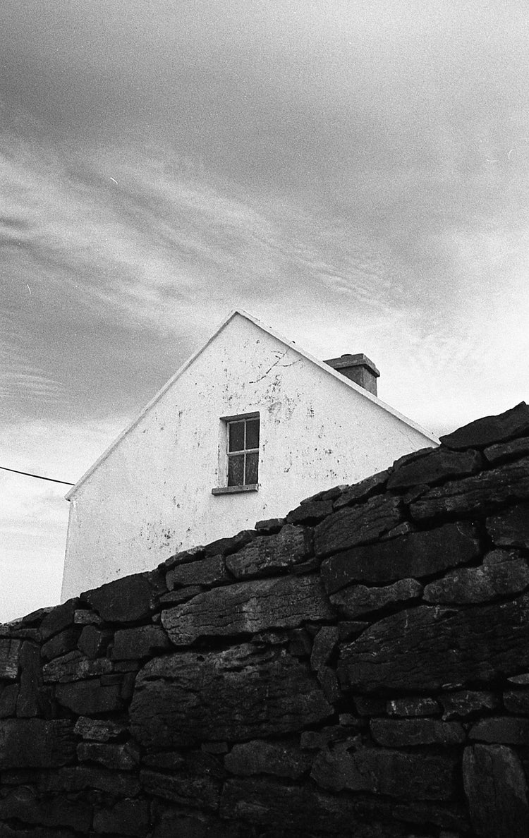 White house with a chimney behind a stone wall under a cloudy sky