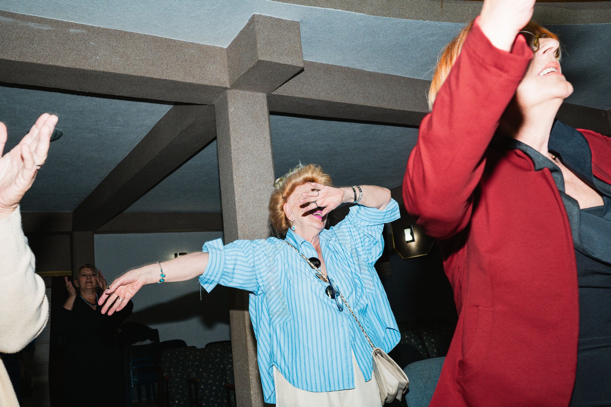 Woman in blue shirt and red jacket interacting with people in a social setting.