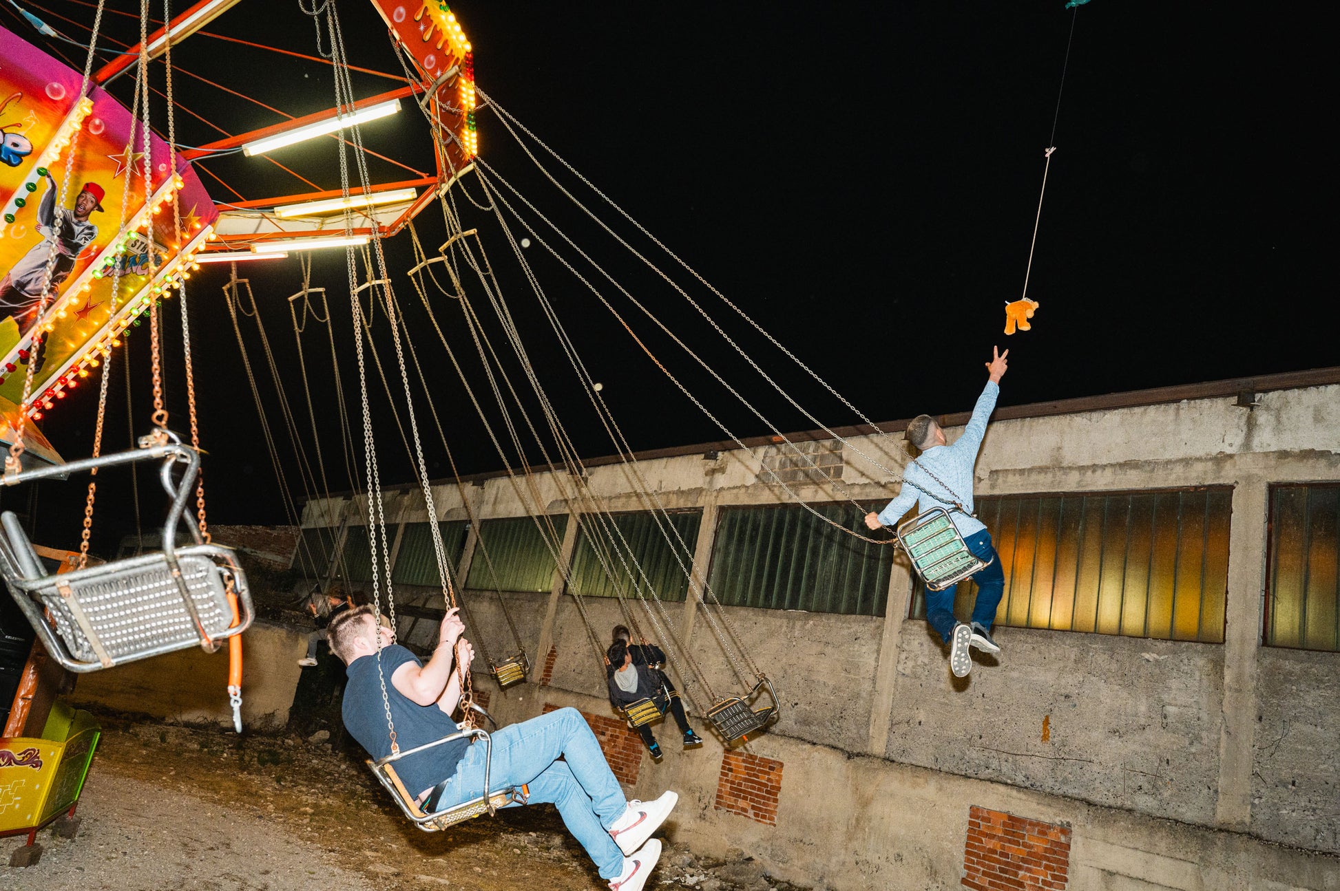 People on a swing ride at night with a dark sky and concrete wall in the background.