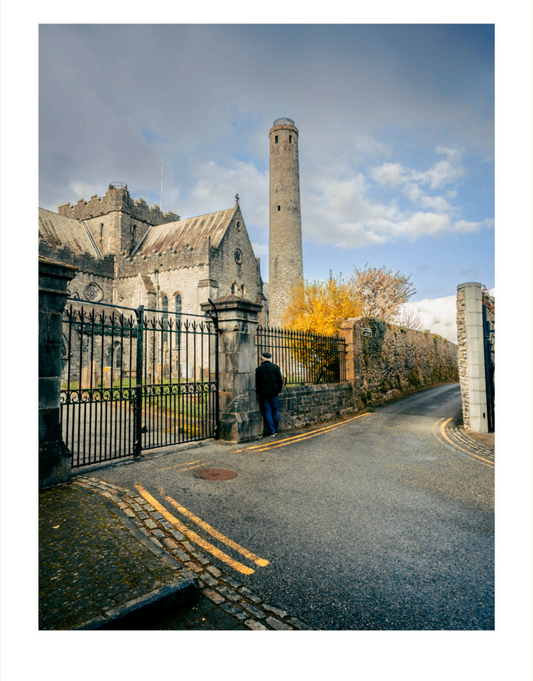 Person standing near a large stone building with a tall tower under a blue sky.