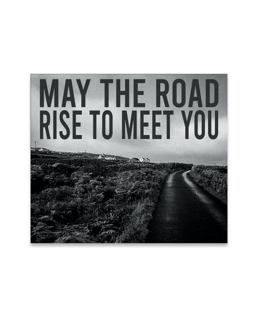 Black and white landscape with a road leading into the distance, featuring the text 'May the road rise to meet you'.